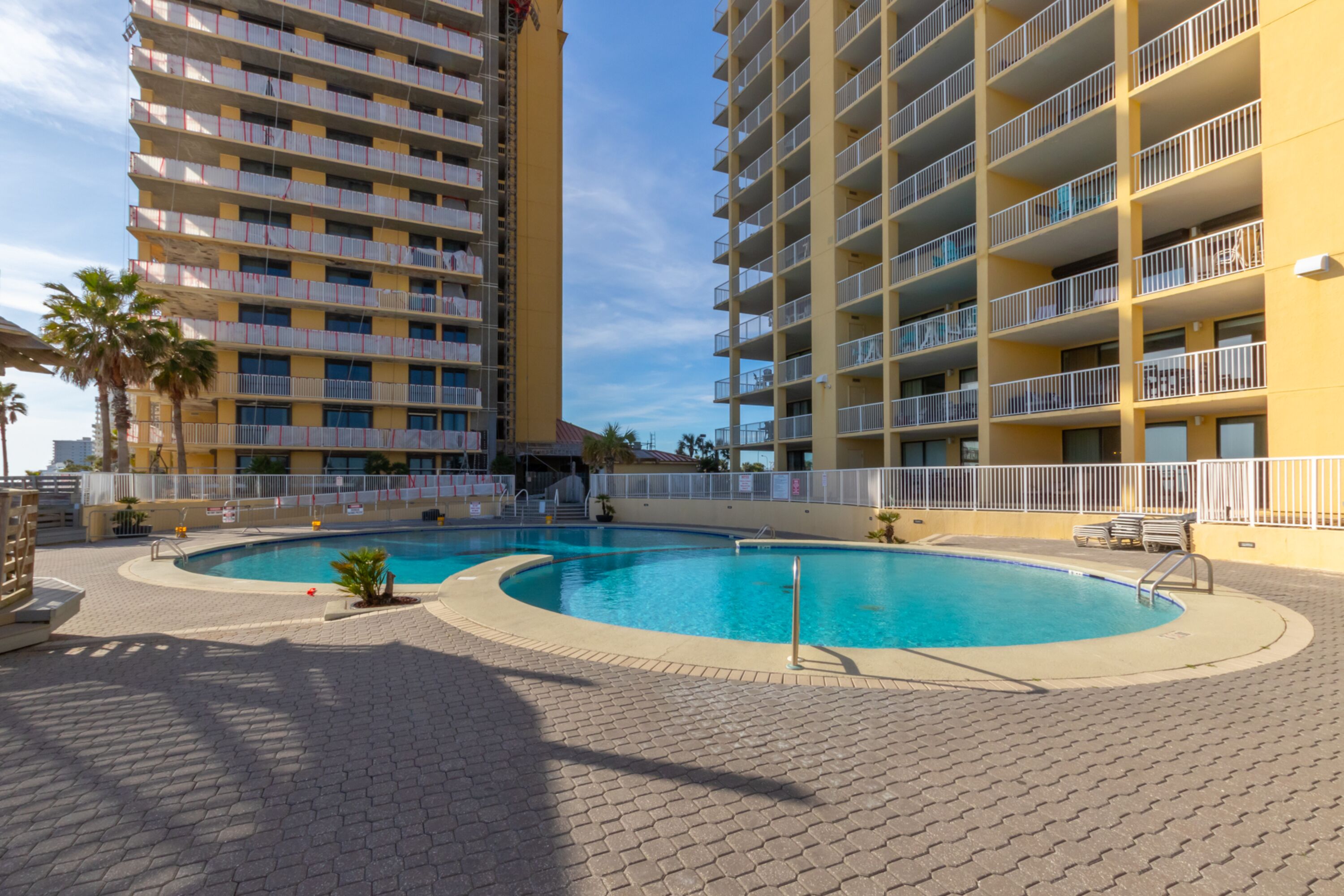 Un hotel con piscina, varios balcones y una palmera.