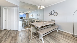 A dining area with a wooden table, benches, and chairs. There is a bicycle mounted on the wall and a door leading to another room. - Summer House 1105A (Orange Beach)