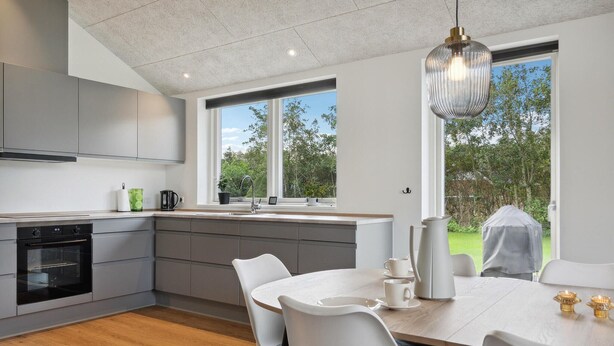 Una cocina moderna con horno integrado, un comedor con mesa y sillas, y ventanas amplias que ofrecen vistas al exterior.