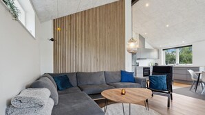 Una sala de estar moderna con un sofá seccional gris, una mesa de centro redonda y una zona de comedor con una silla negra y una mesa blanca.
