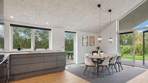 Una cocina moderna con una isla grande, un comedor con mesa y sillas, y ventanas amplias que ofrecen vistas al exterior.