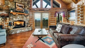 A cozy log cabin interior with a stone fireplace, wooden ceiling, and a leather couch.