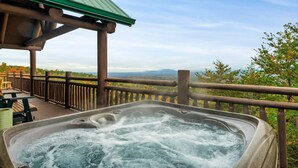 A hot tub on a wooden deck with a view of trees and mountains.