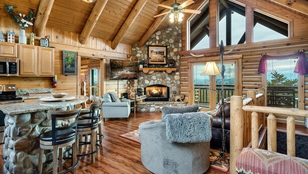 A log cabin interior with a stone fireplace, wooden ceiling beams, and a stone bar counter.