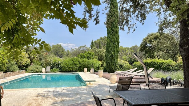 A swimming pool with lounge chairs and a table, surrounded by greenery and trees. - Villa Maya : Large villa and amazing pool in Luberon (Mérindol)