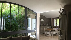A living room with a sofa, a dining area with a table and chairs, and a kitchen area with cabinets and a window. - Villa Maya : Large villa and amazing pool in Luberon (Mérindol)