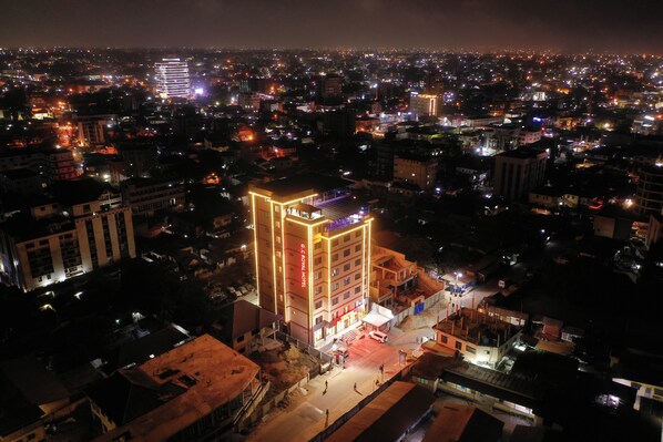 A hotel with a prominent, illuminated facade, surrounded by a densely populated urban area at night. - G.C Royal Hotel (Accra)