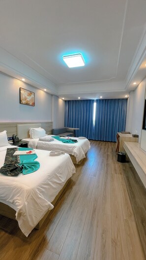 A hotel room with two beds, a desk, a chair, a flat-screen TV, and a window with blue curtains. - G.C Royal Hotel (Accra)