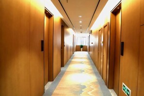 A hotel corridor with wooden doors, a patterned carpet, and a green emergency exit sign. - Songfulou Hotel (Qimen)