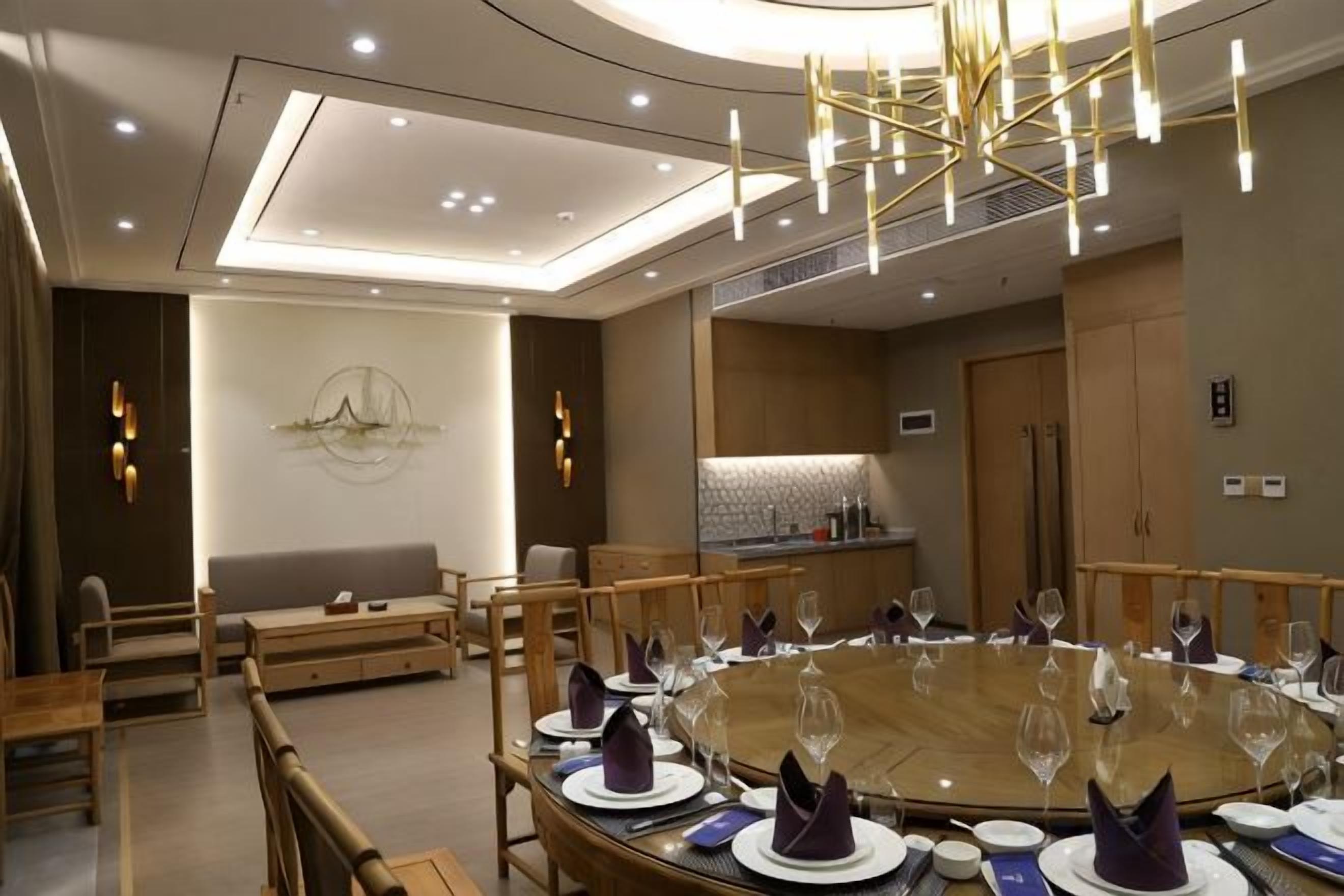 A modern dining area with a round table set for a meal, a sofa, and a kitchen area in the background.