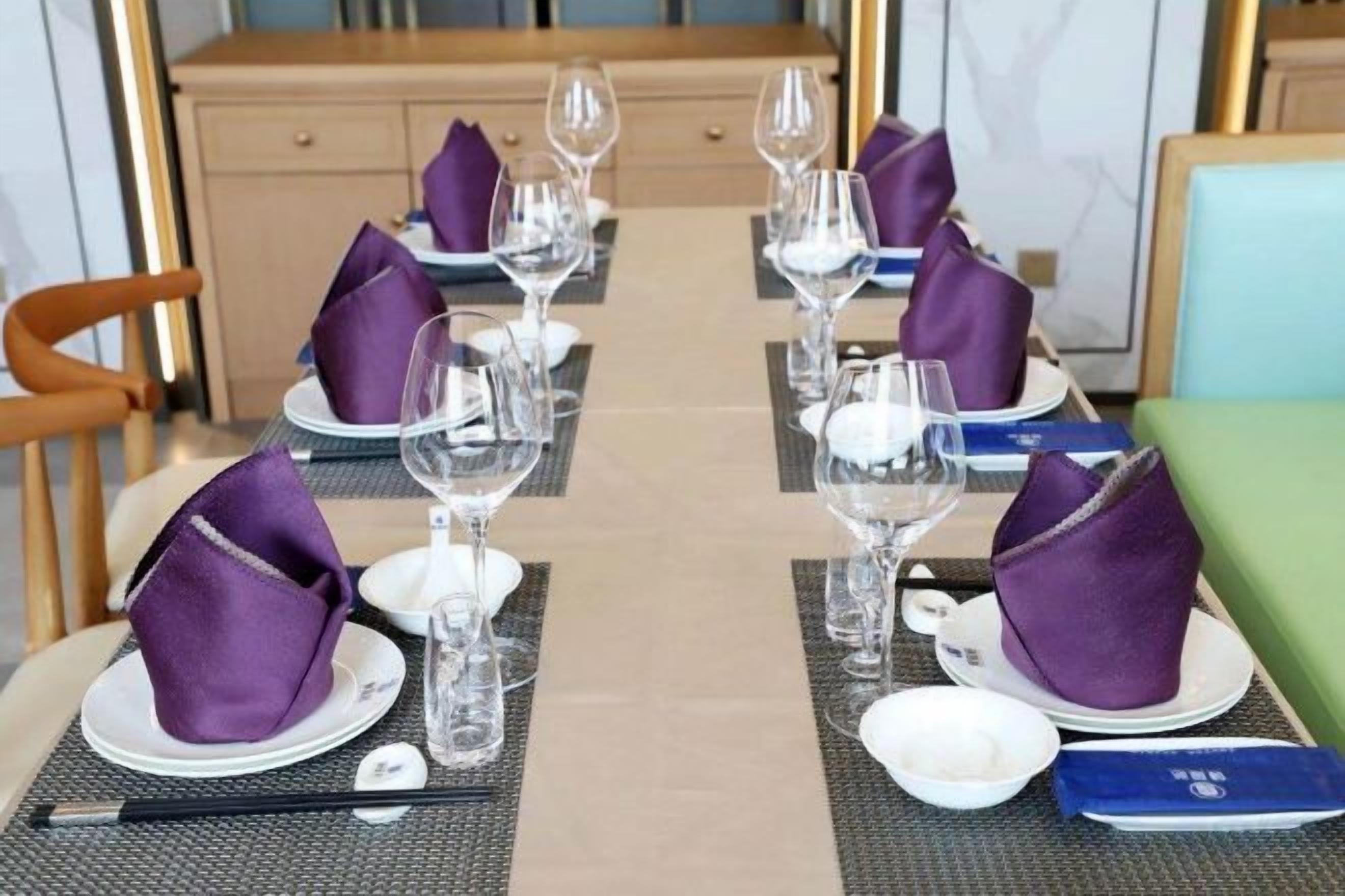 A dining table set with plates, glasses, and purple napkins.