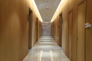 A hotel hallway with wooden doors, a marble floor, and recessed lighting.