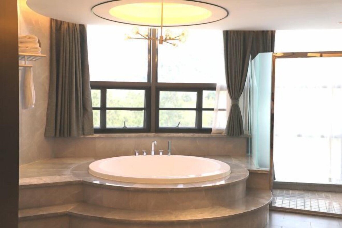 A bathroom with a freestanding bathtub, a chandelier, and a view through a large window.