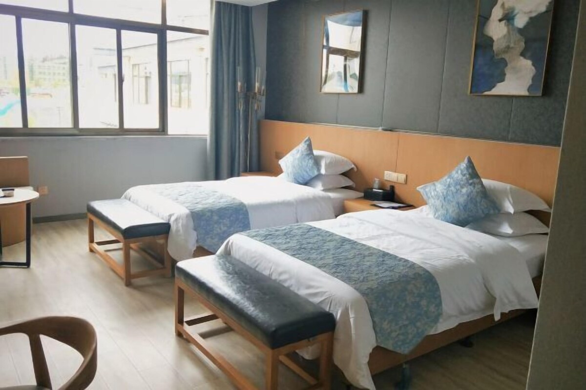 A hotel room with two beds, a bench, a desk, and a window with curtains.
