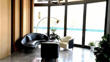 Un vestíbulo moderno con un sofá negro curvo, un sillón blanco, un reposapiés negro y una planta en maceta.
