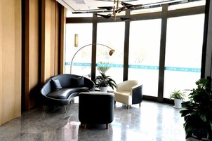 Un vestíbulo moderno con un sofá negro curvo, un sillón blanco, un reposapiés negro y una planta en maceta.