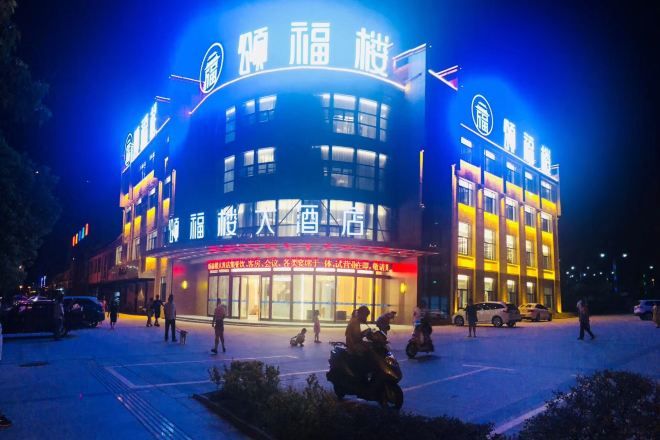 A building with illuminated signage, a parking lot, and people walking around.