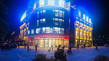 A building with illuminated signage, a parking lot, and people walking around.