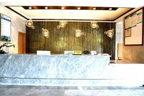 A reception area with a marble counter, hanging pendant lights, and a vertical wooden panel wall. - Songfulou Hotel (Qimen)