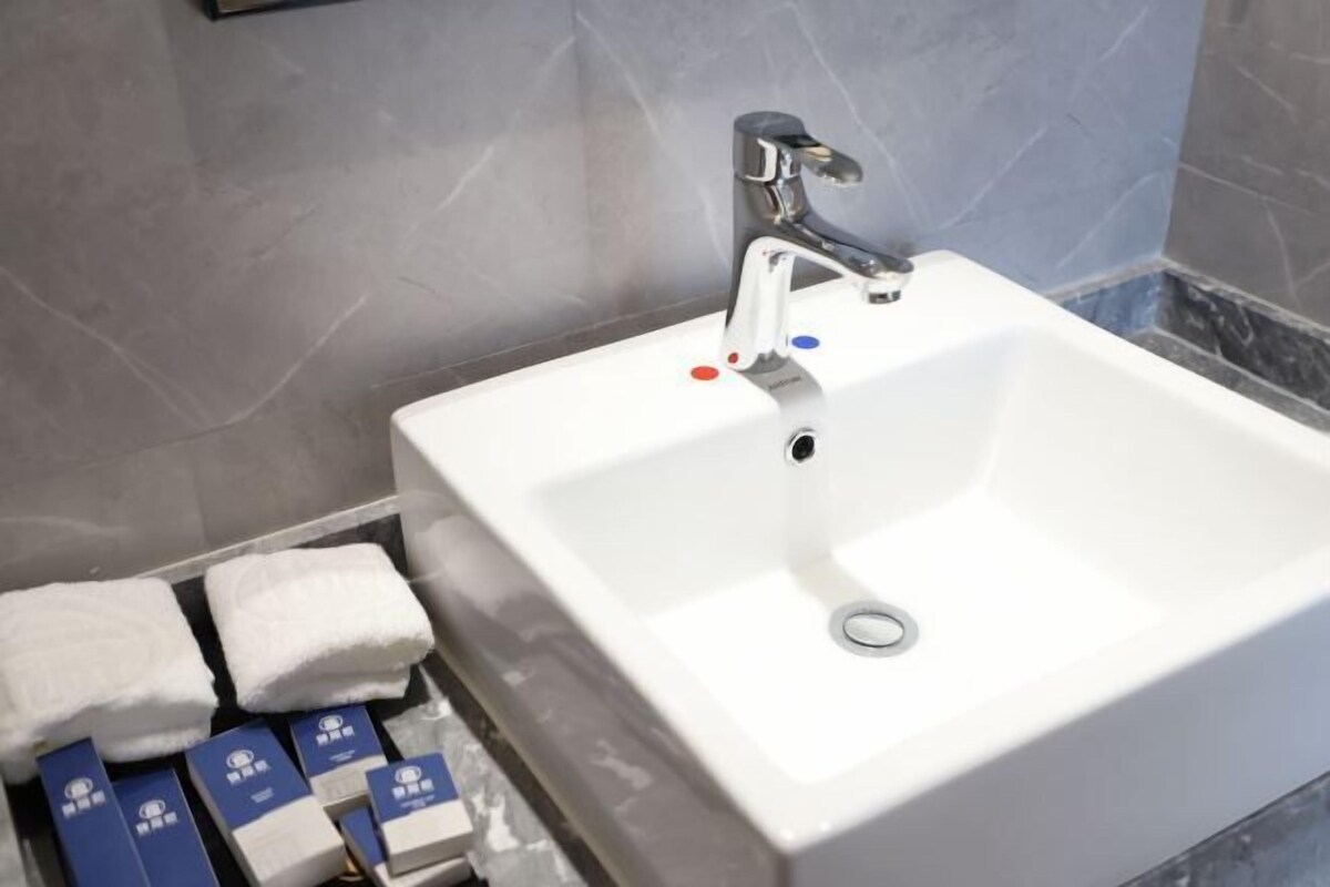 A bathroom with a white sink, a chrome faucet, and a marble backsplash. There are towels and toiletries on the counter.