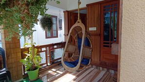 Een veranda met een hangstoel, een bloempot en een houten leuning.