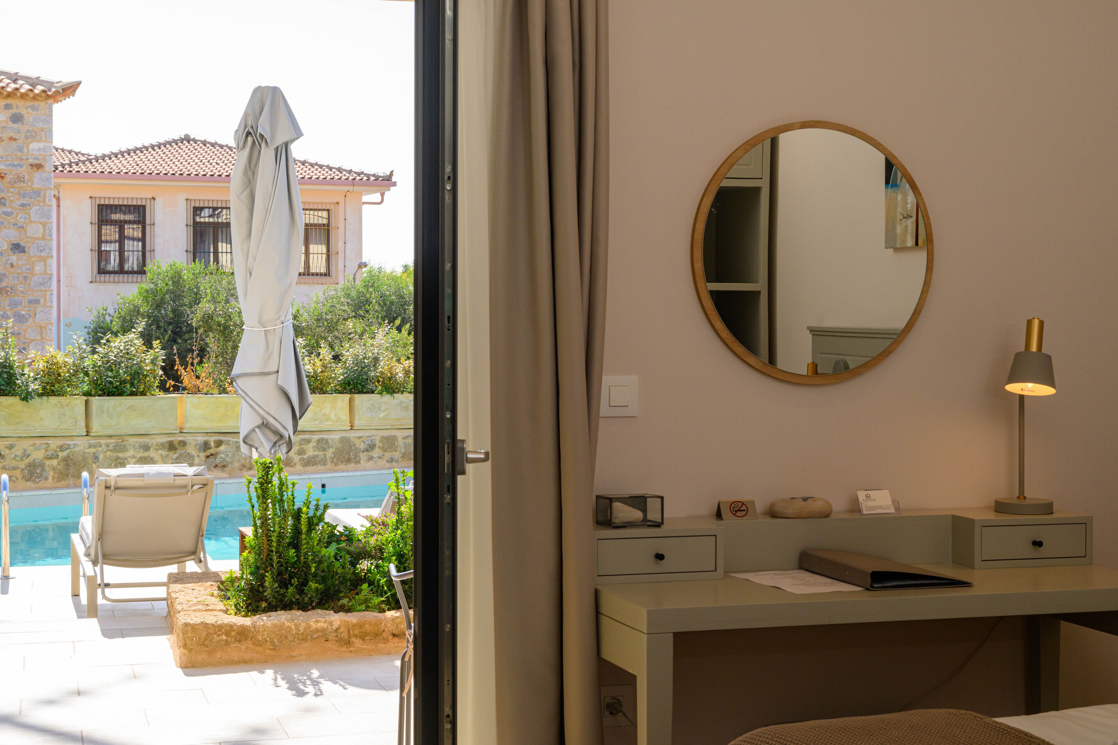 A hotel room with a pool view, a desk with a lamp, a mirror, and a chair.