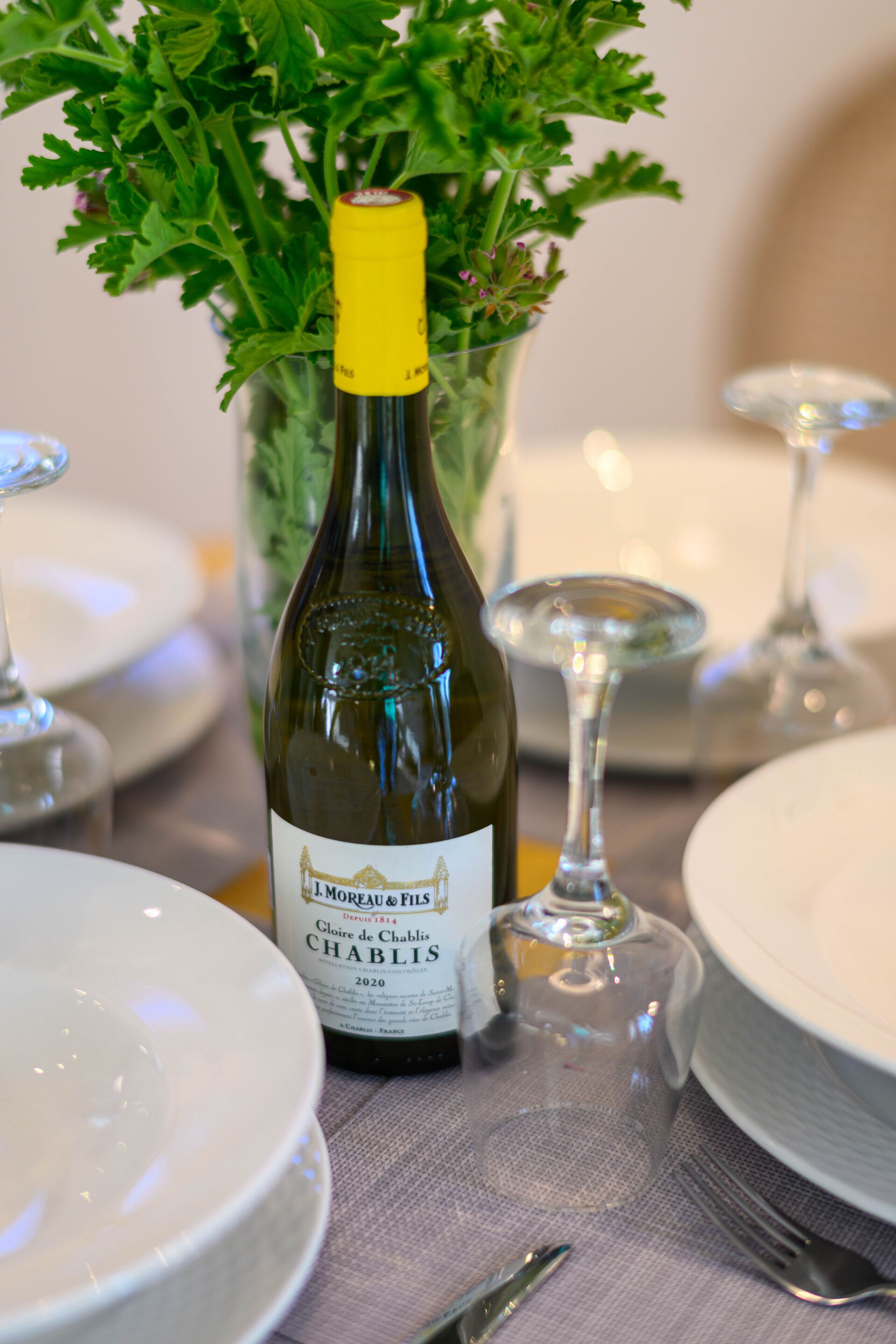 Une bouteille de vin avec une étiquette, entourée d’assiettes et d’un verre sur une table.