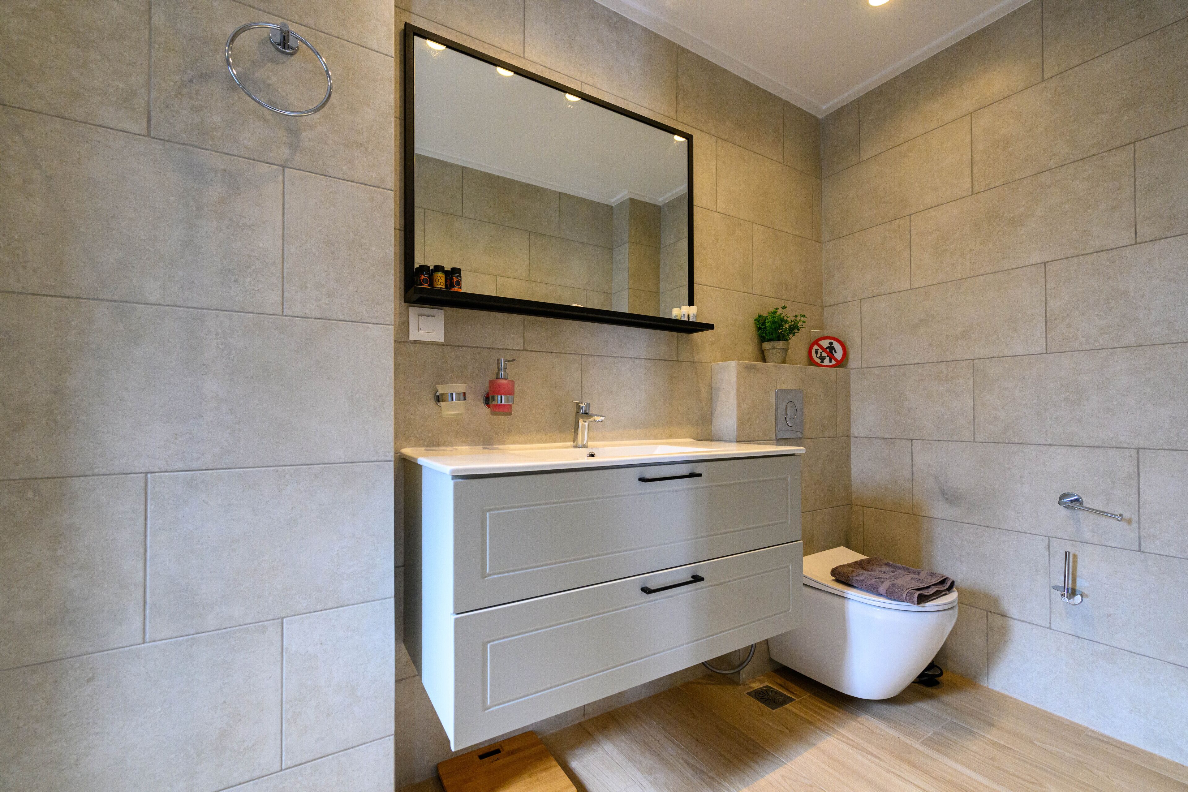 A modern bathroom with a white vanity, a large mirror, and a toilet.