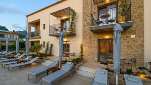 A hotel courtyard with sun loungers, outdoor seating, and a stone building with balconies. - Kannas Mani-Luxury Suites- Adults friendly 14+ (West Mani)