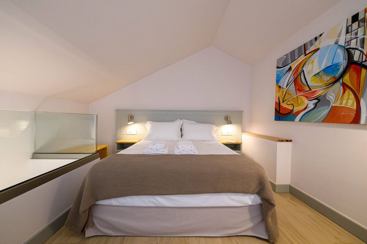 Een moderne hotelkamer met een groot bed, een nachtkastje, een spiegel en een kleurrijk abstract schilderij aan de muur.