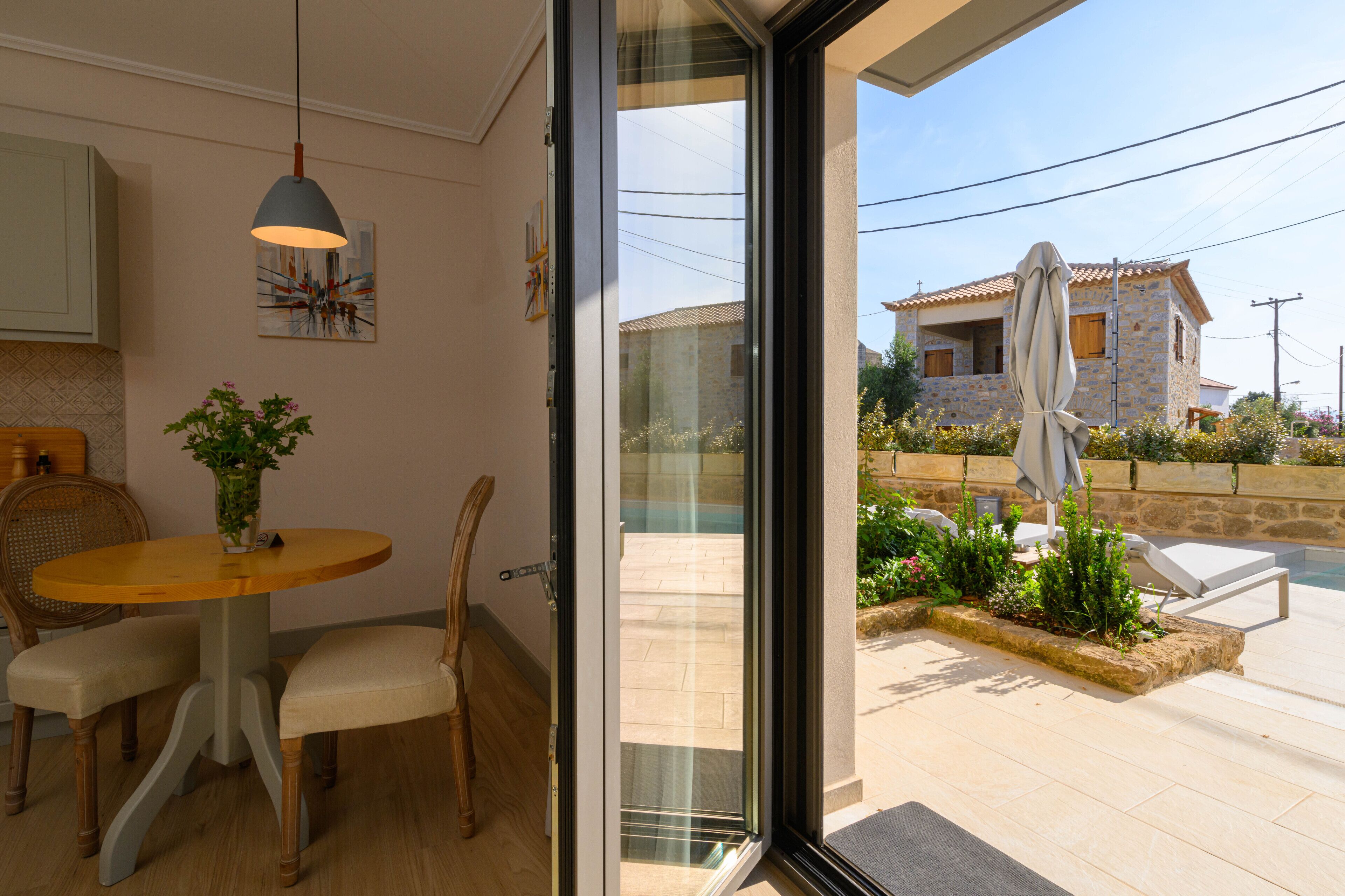 A modern kitchen with a dining area, a large sliding glass door leading to a poolside with lounge chairs.