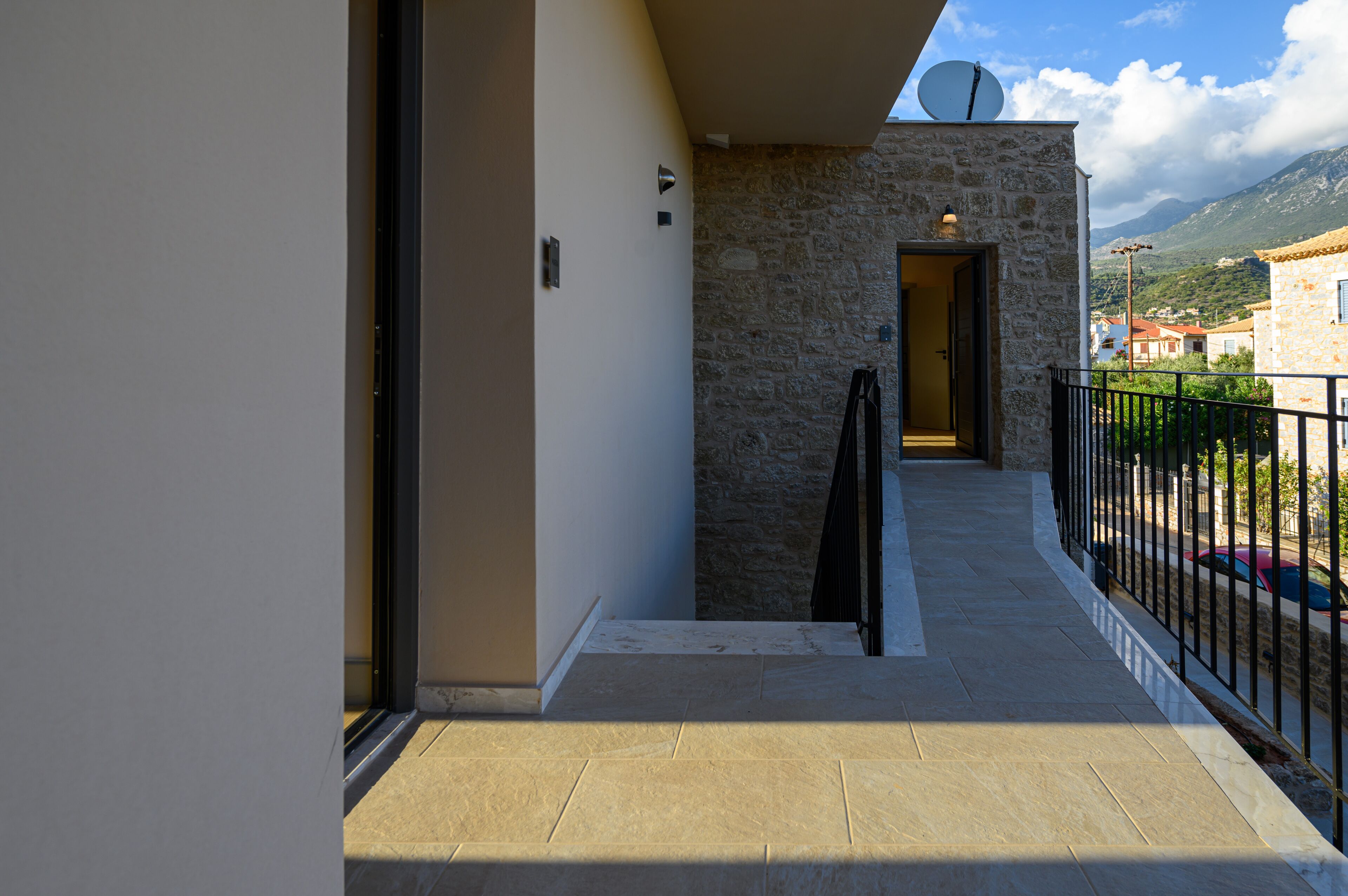 A balcony with stone walls, a door leading to an interior room, and a view of a mountainous landscape.