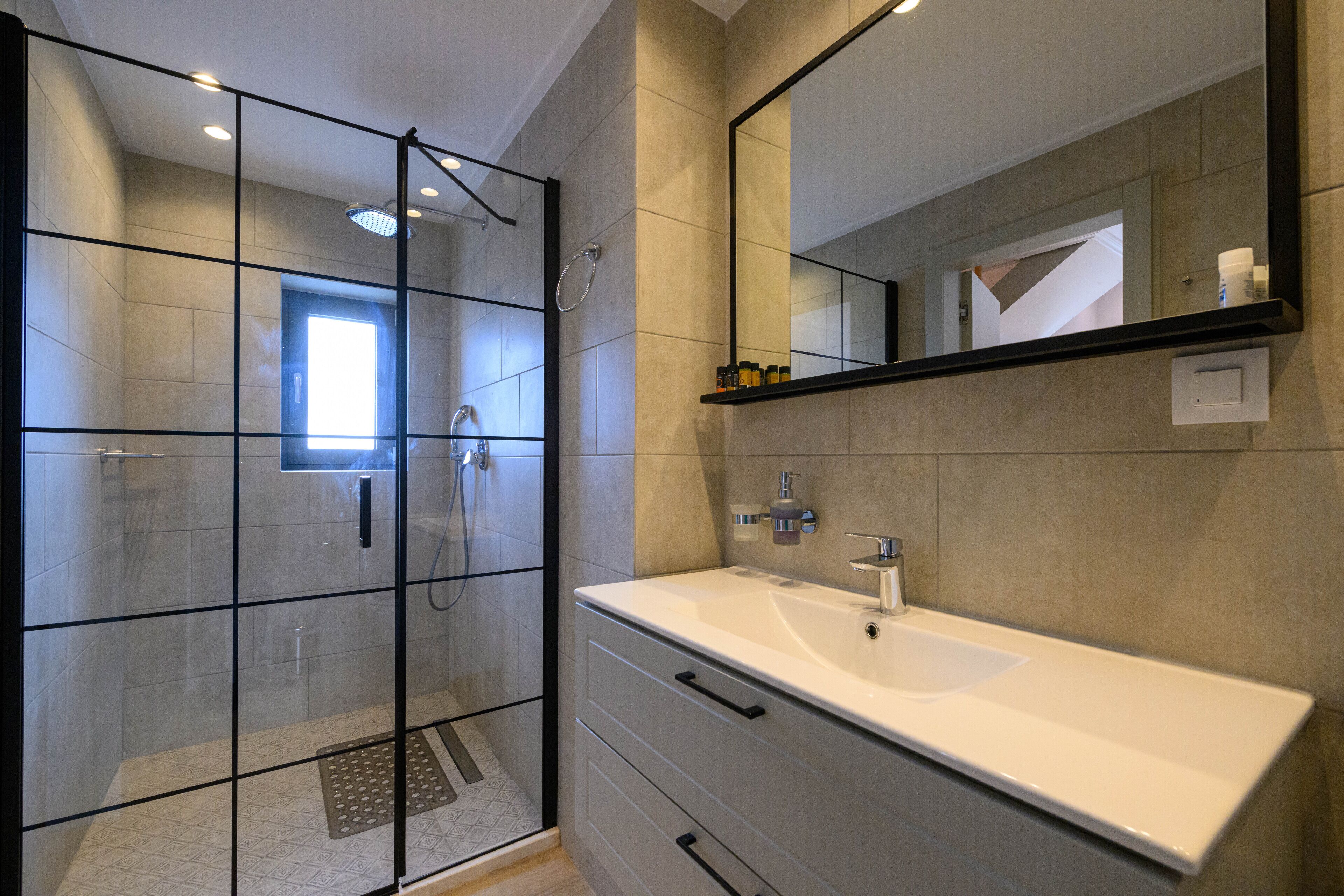 A modern bathroom with a glass-enclosed shower, a white sink, and a large mirror.