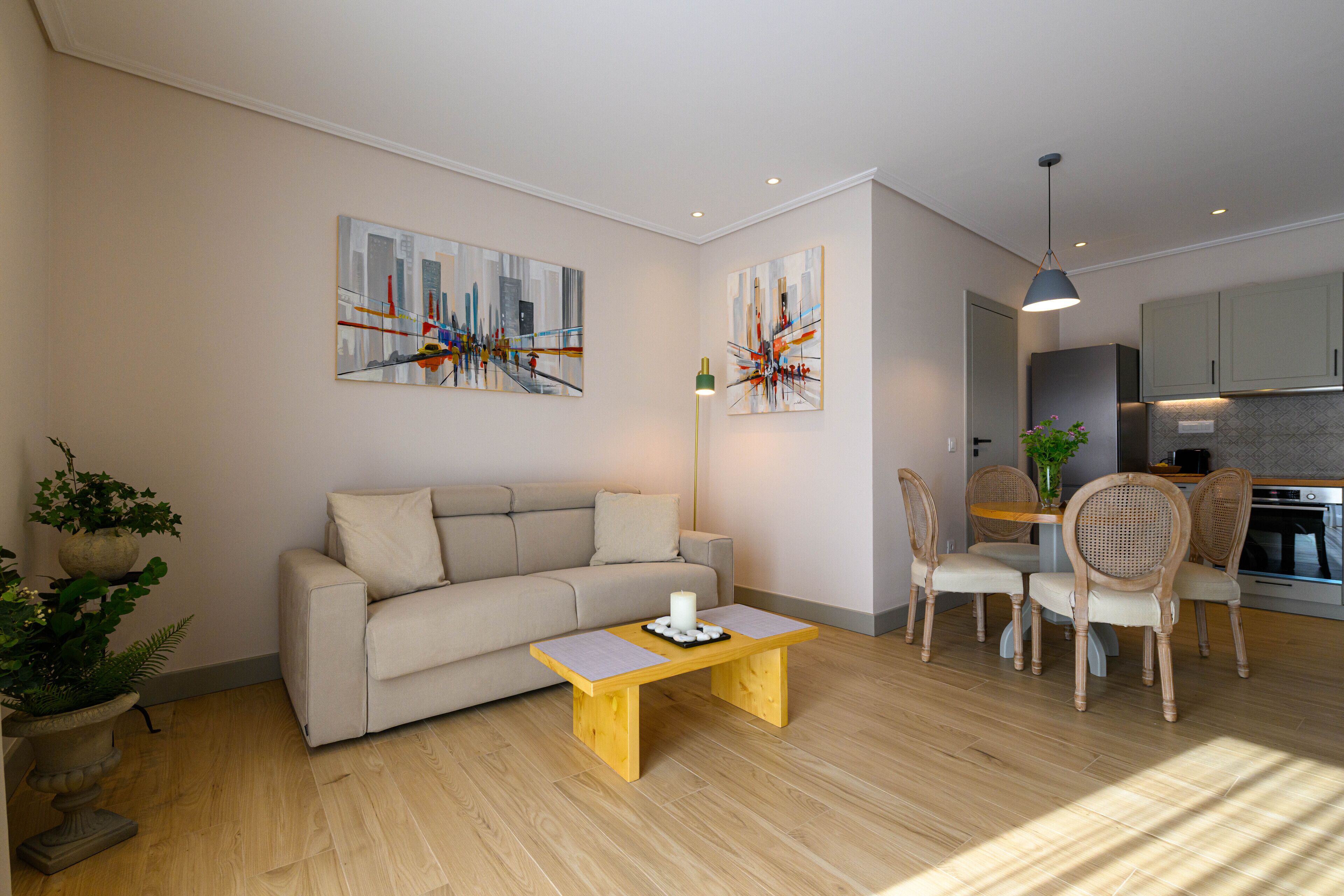 Ein modernes Wohnzimmer mit einer Couch, einem Couchtisch und einem Essbereich mit Stühlen. An den Wänden befinden sich abstrakte Gemälde und ein Blumentopf.