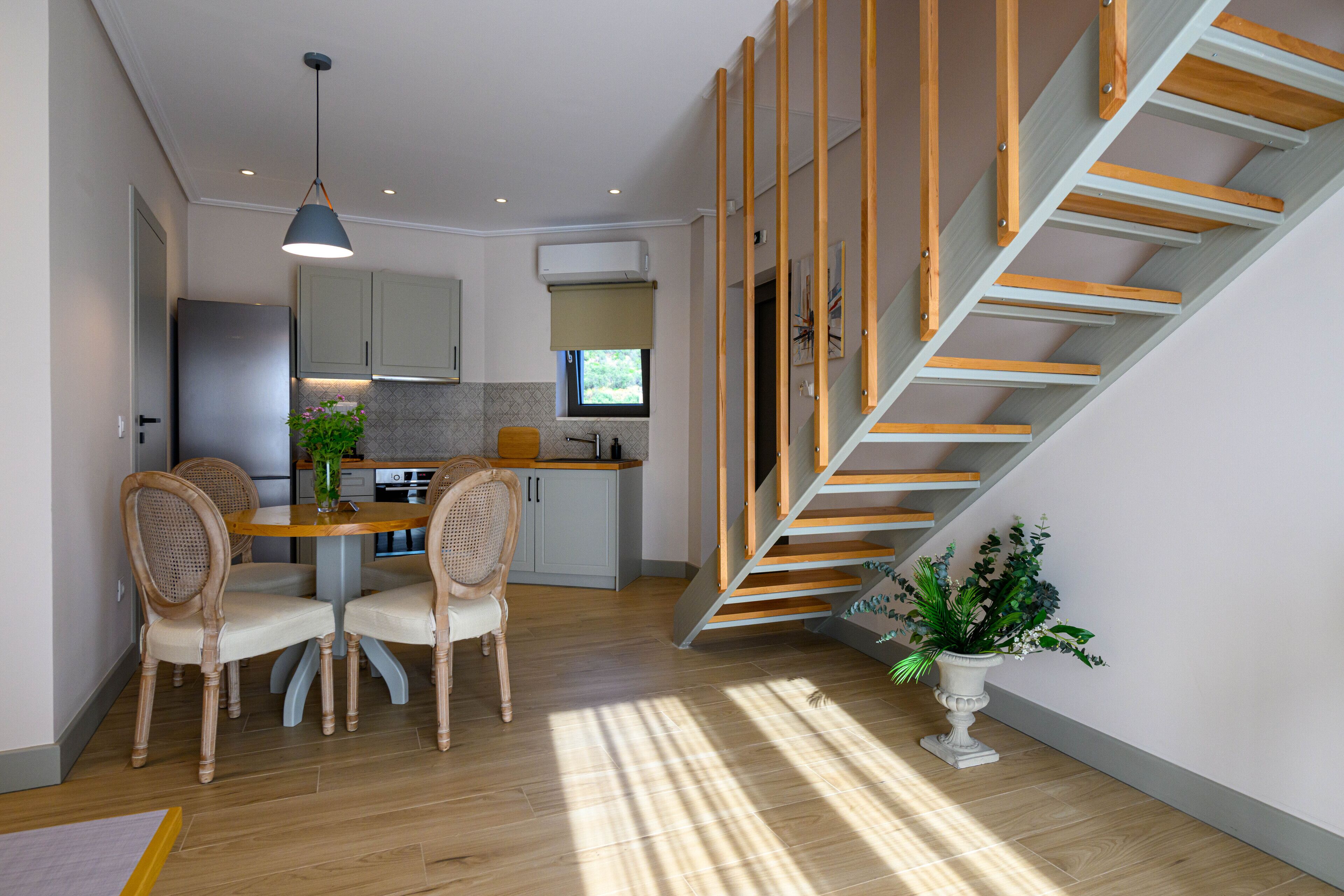 A modern kitchen with a dining area, wooden staircase, and a potted plant.