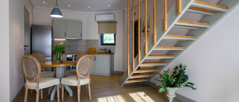 A modern kitchen with a dining area, wooden staircase, and a potted plant.