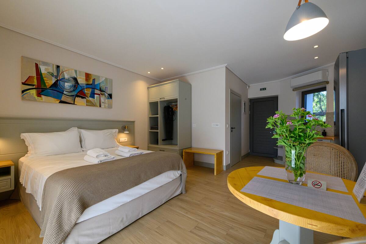 Een moderne hotelkamer met een bed, nachtkastje, bureau, stoel, een vaas met bloemen en een schilderij aan de muur.