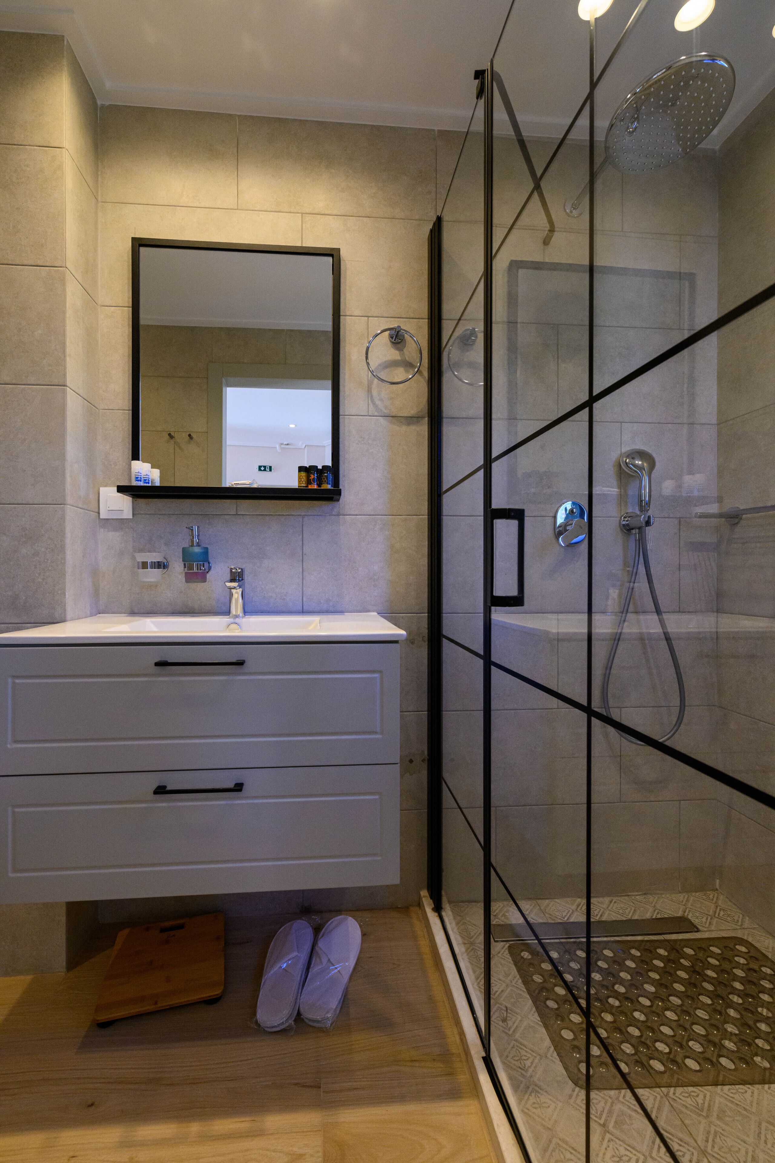 A modern bathroom with a glass shower enclosure, a white sink, and a mirror above it.