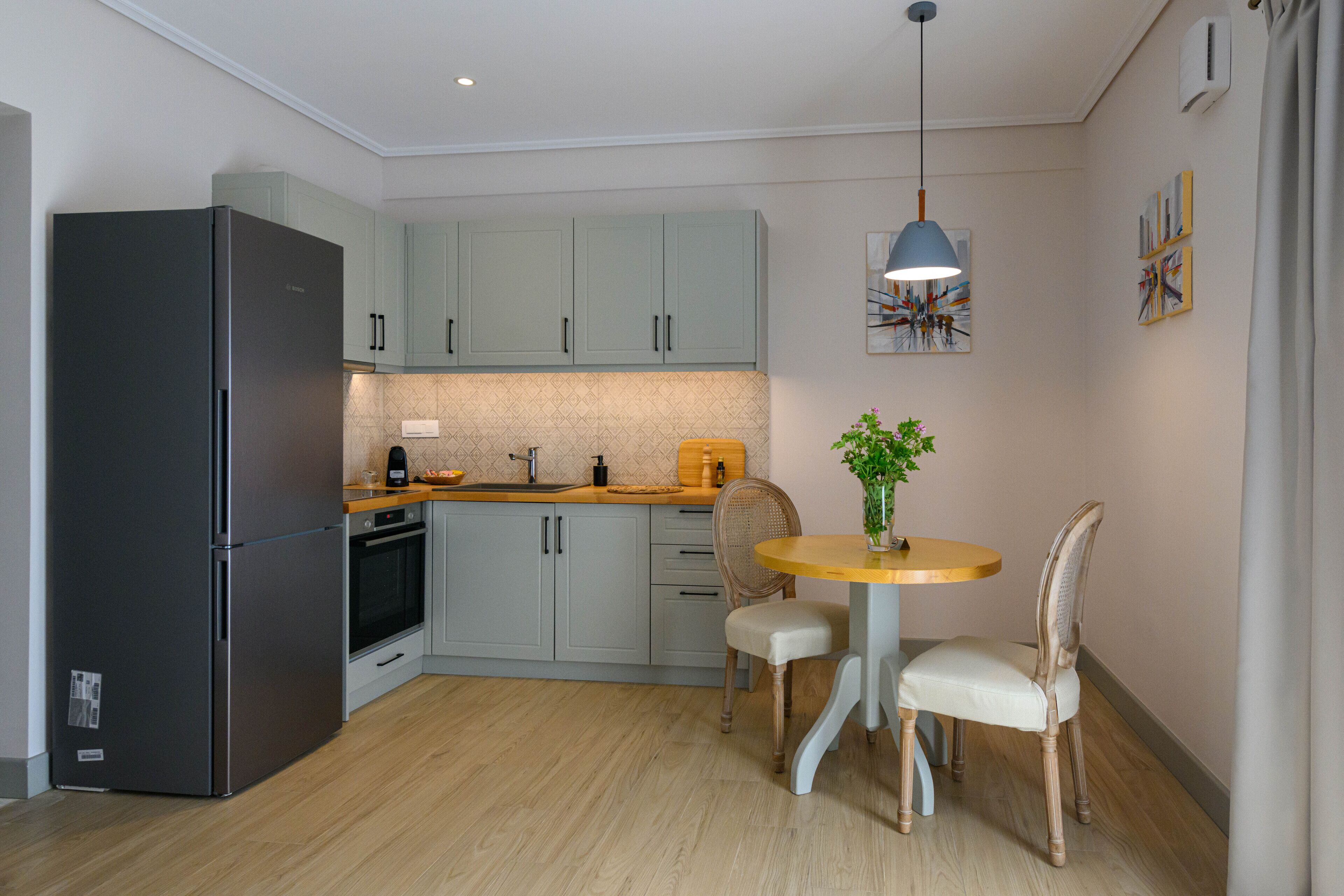 Una cocina moderna con armarios grises, un refrigerador negro, una encimera de madera y un comedor con una mesa redonda y dos sillas.