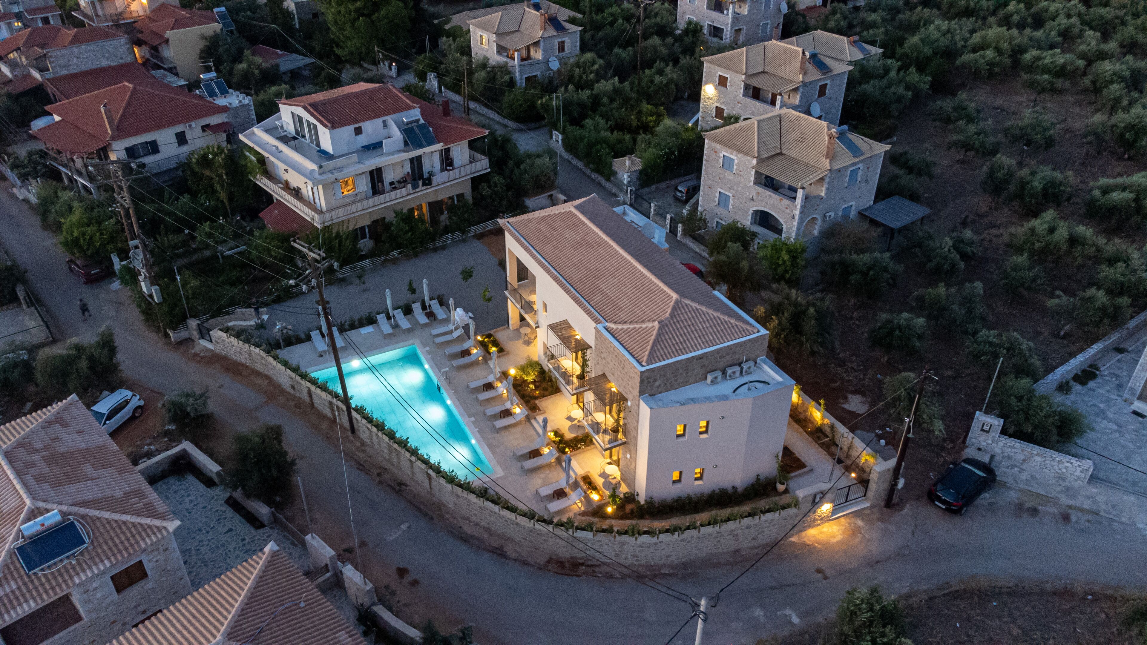 An aerial view of a residential area with a house featuring a swimming pool, multiple balconies, and a stone wall surrounding the property.