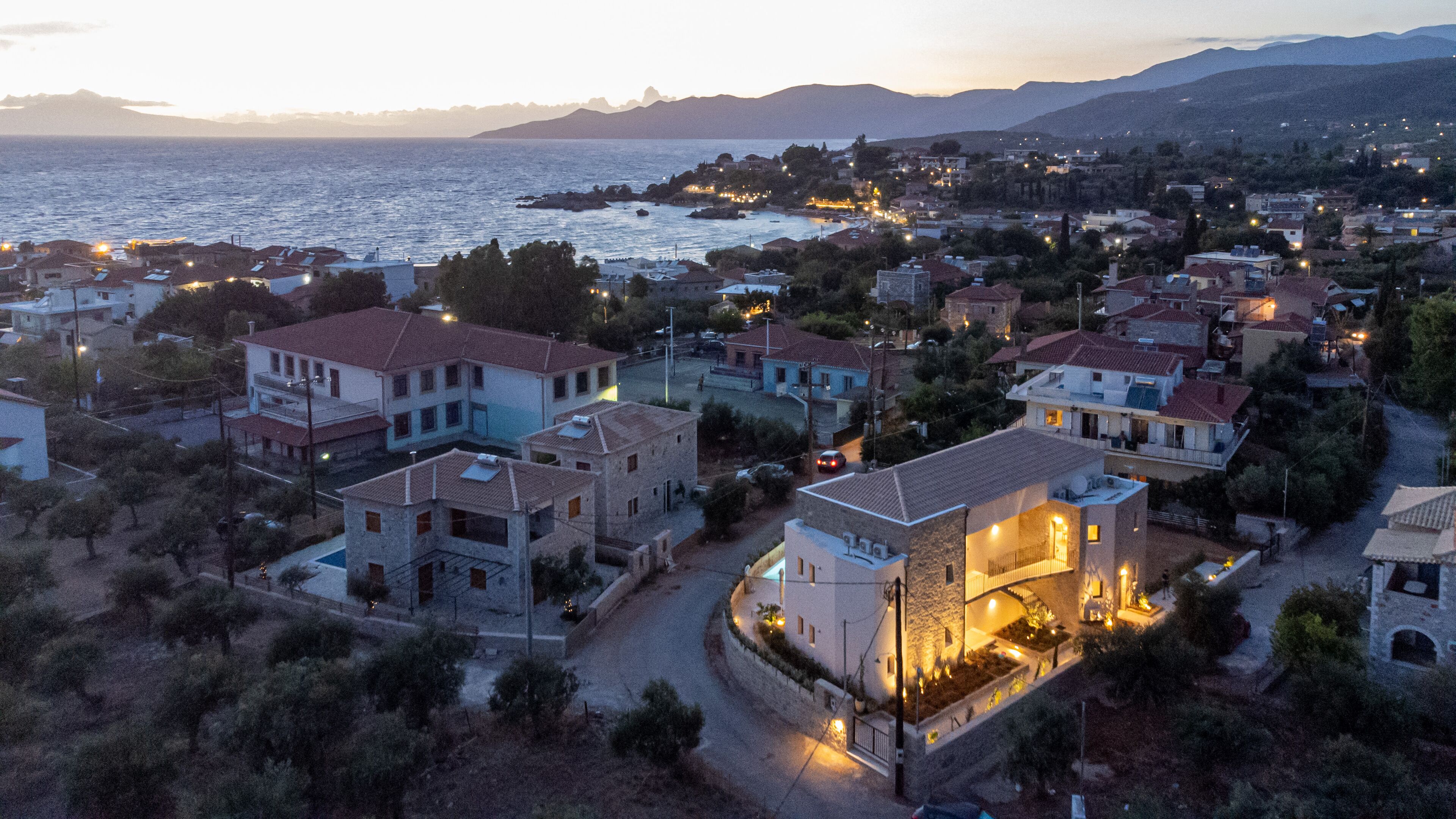A coastal town with houses, a sea view, and a mountainous backdrop.