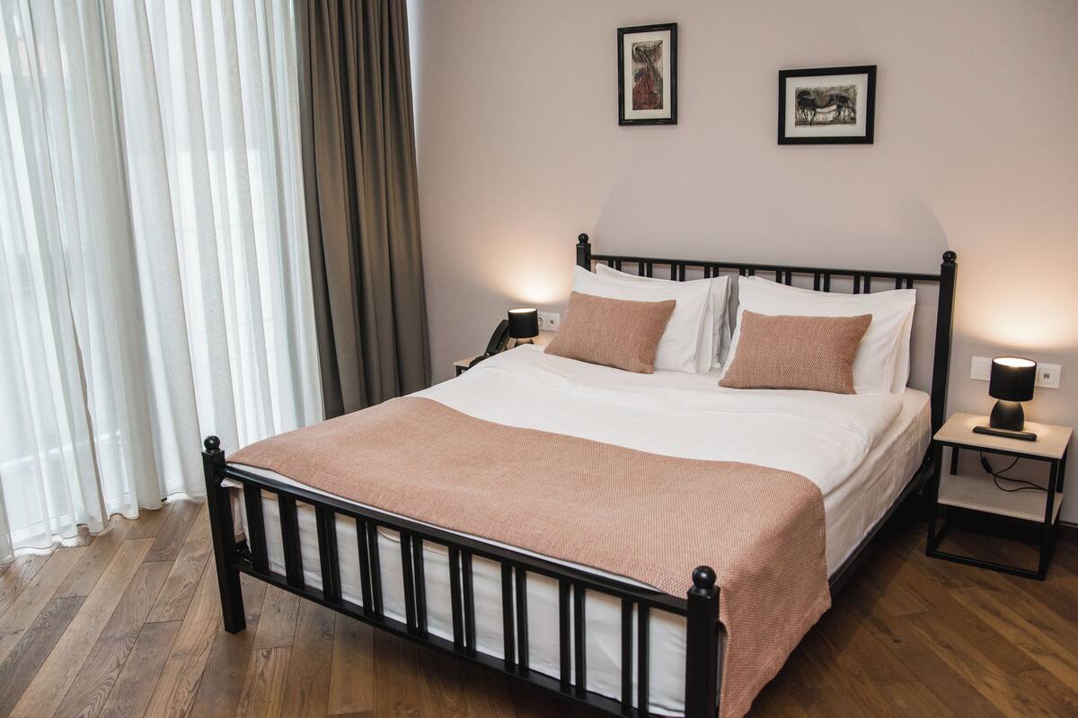 A neatly made bed with a brown blanket, a bedside table with a lamp, and two framed pictures on the wall.