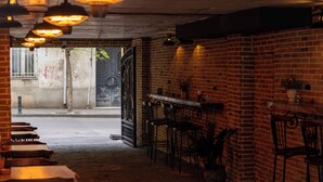 Interior com pouca luz, paredes de tijolo, cadeiras de metal e luminárias pendentes.