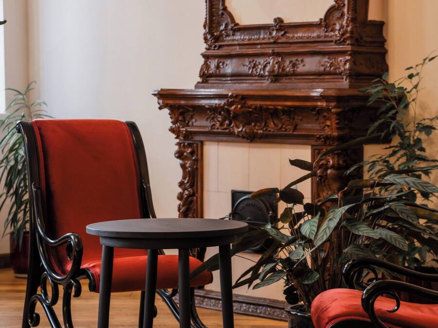 Una habitación con piso de madera, un sillón tapizado en rojo, una pequeña mesa redonda y un espejo grande con detalles decorativos.