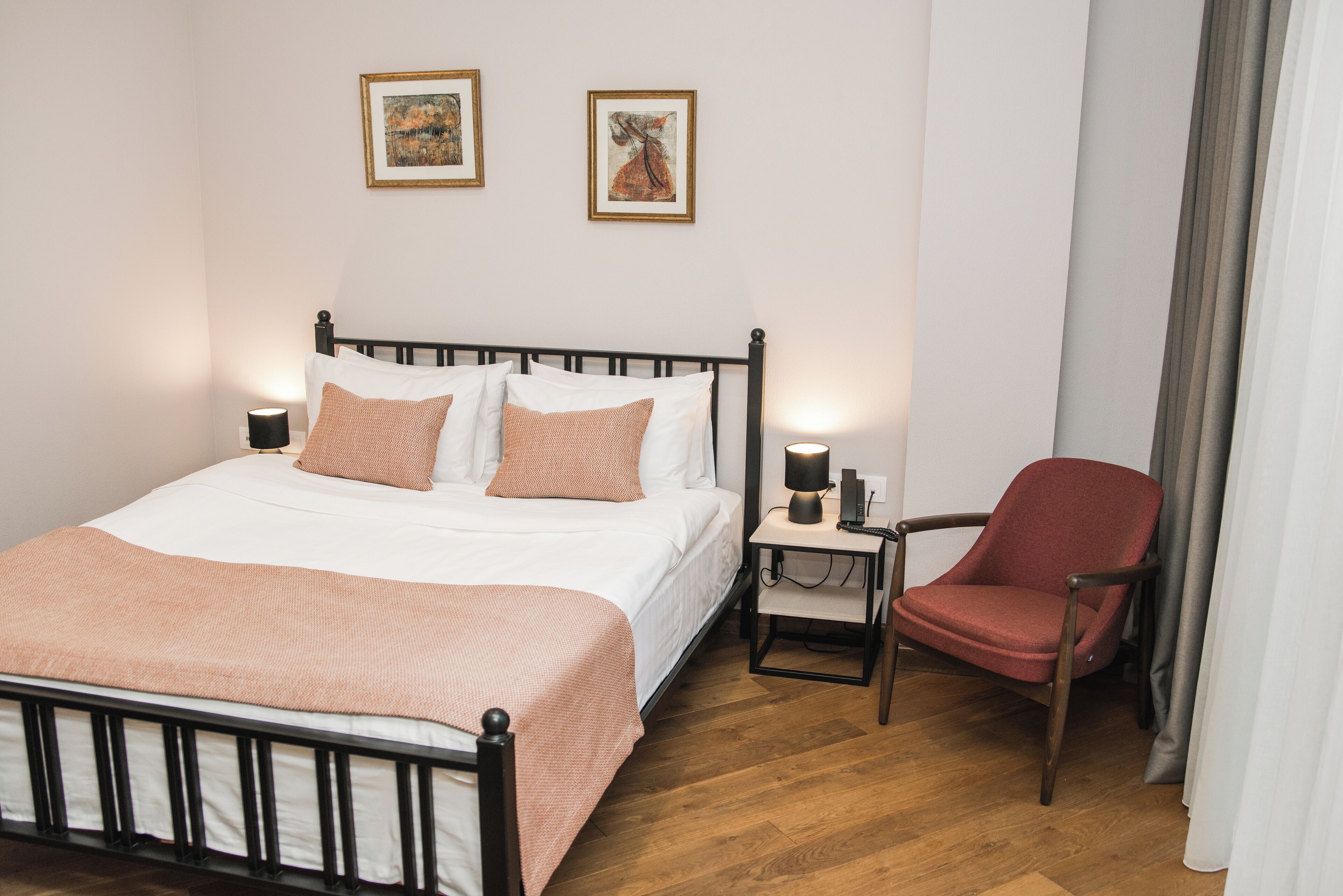 Une chambre à coucher bien rangée, avec un lit, des lampes de chevet, une chaise et deux tableaux encadrés accrochés au mur.