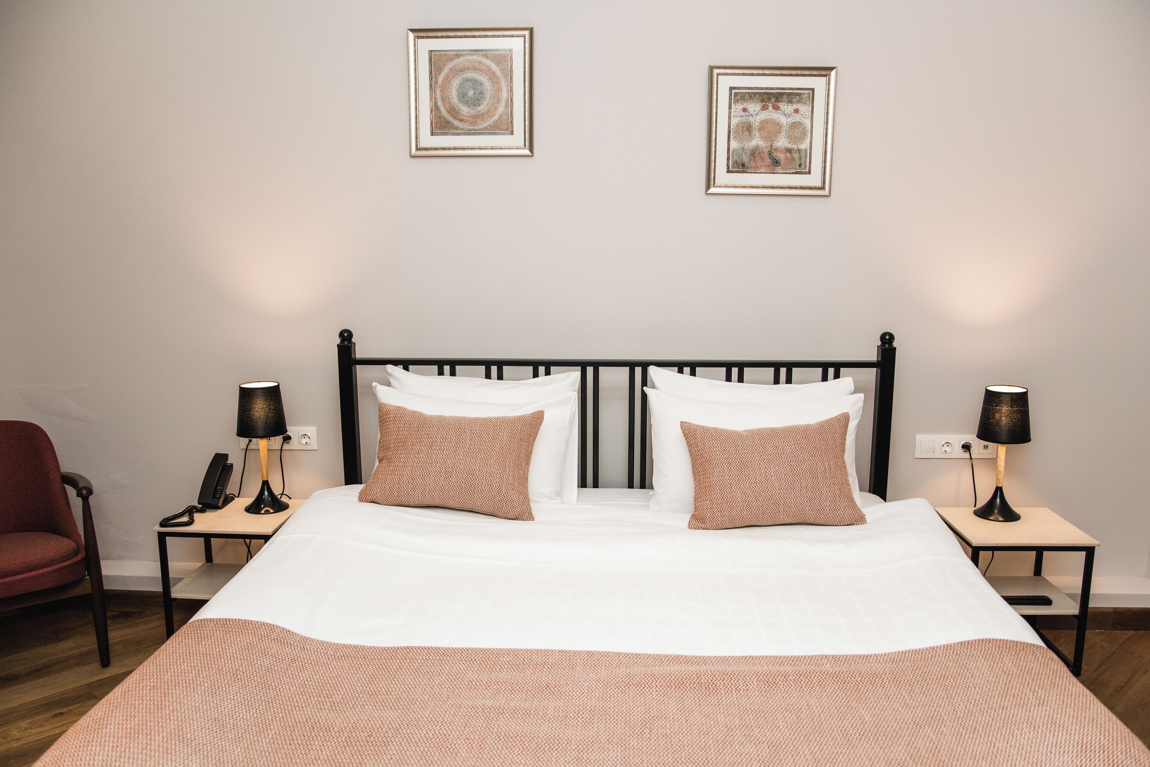 Een netjes opgemaakt bed met wit en bruin beddengoed, twee nachtkastjes met lampen en twee ingelijste foto's aan de muur.