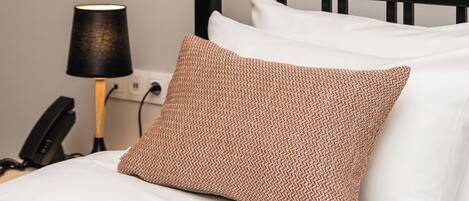 A neatly made bed with white and brown pillows, a black metal headboard, a bedside lamp, and a phone on the nightstand.