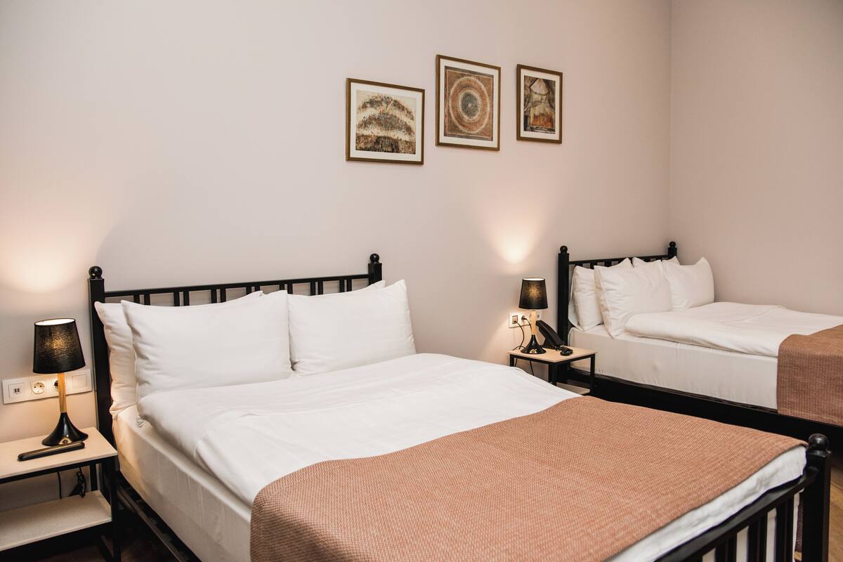 A hotel room with two beds, a nightstand with a lamp, and three framed pictures on the wall.