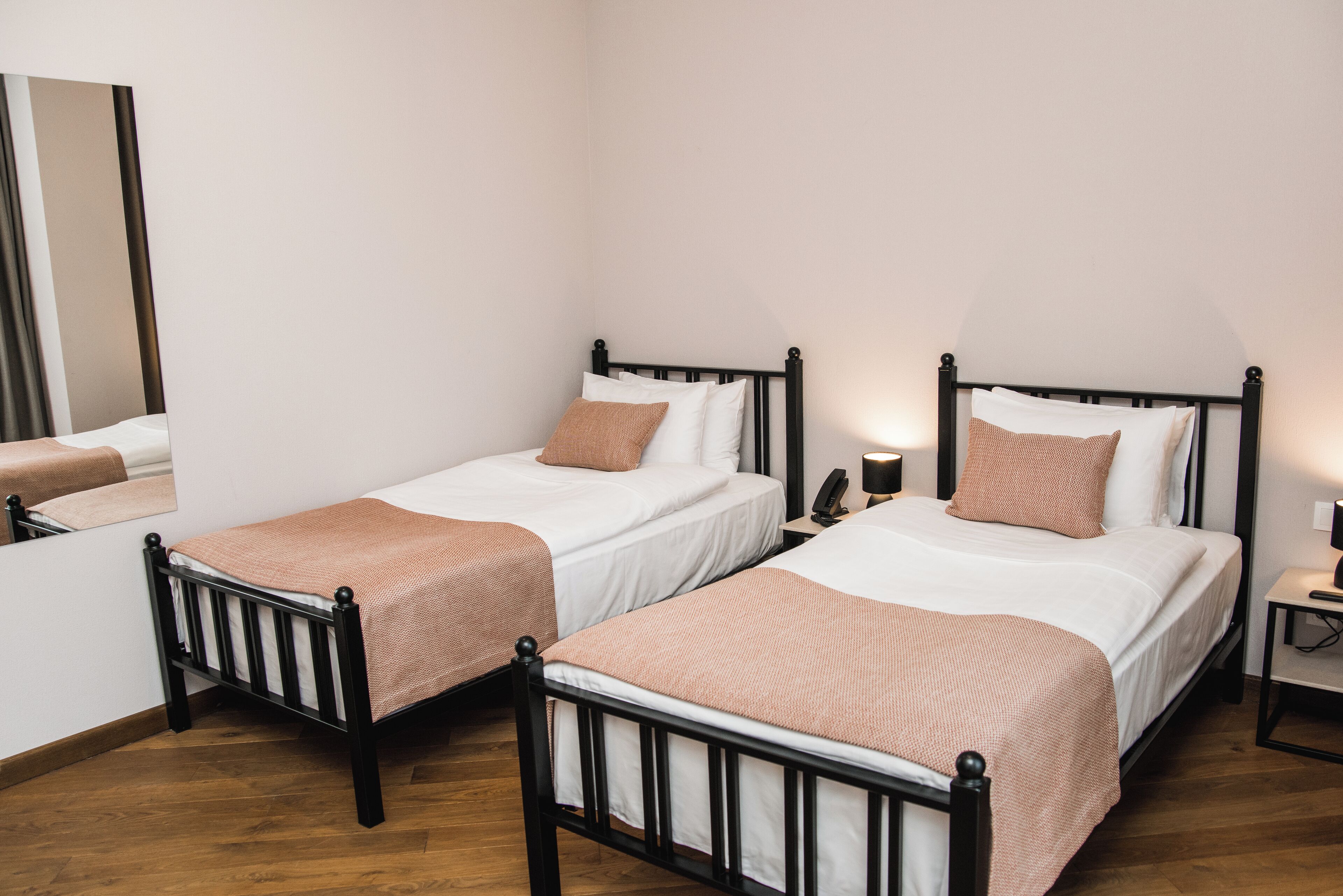 Habitación de hotel con dos camas individuales, cada una con un colchón blanco y una manta marrón. A cada lado de las camas hay una mesita de noche con una lámpara.