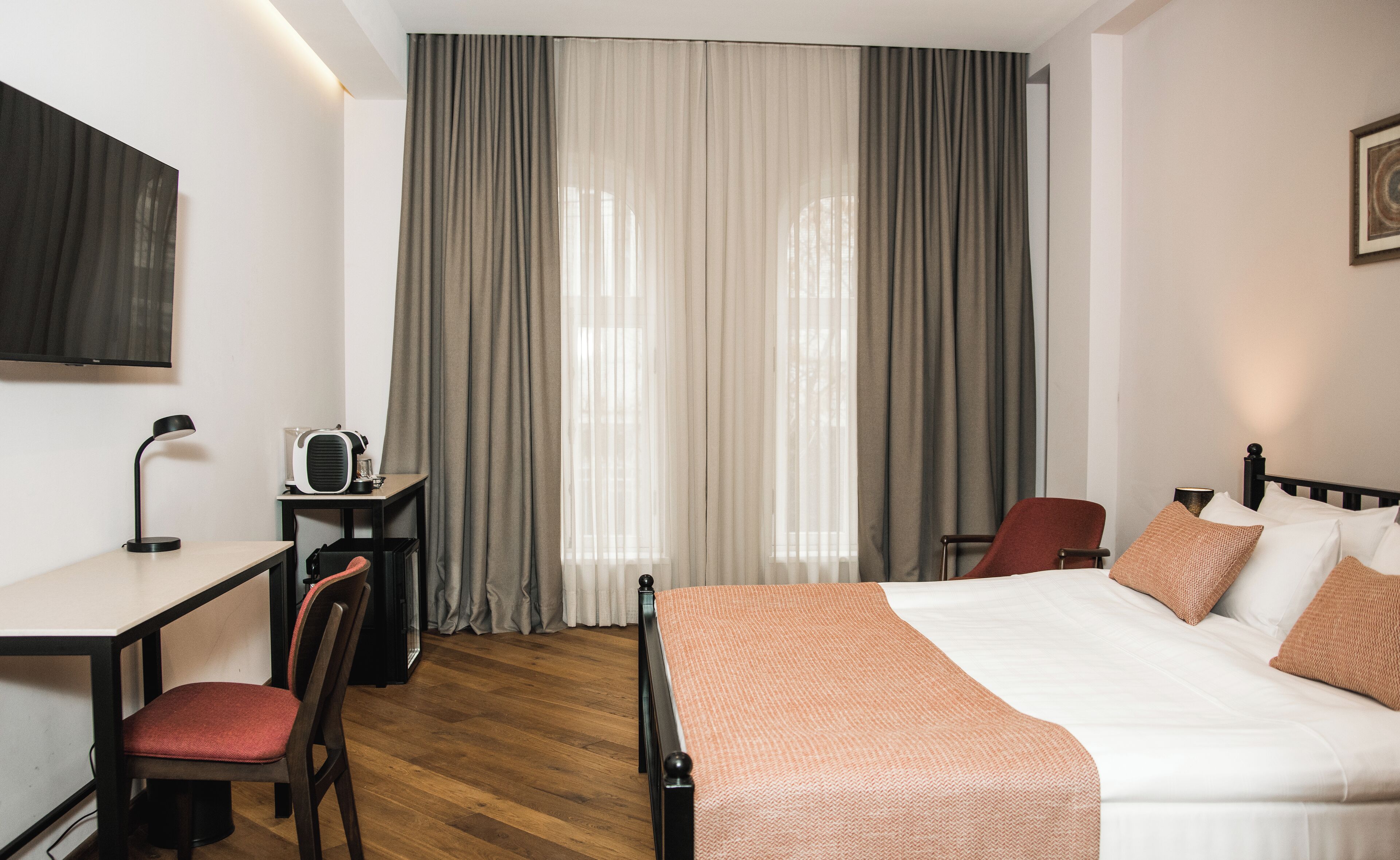 A hotel room with a bed, a desk, a chair, a TV, and curtains.
